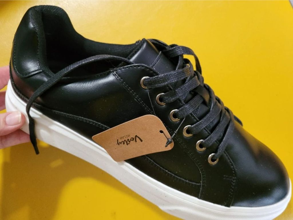 A hand holding a Vostey Men's Fashion Sneakers in black
