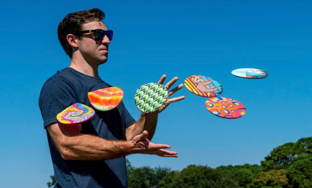 Man, standing with sunglasses and tons of flying silicone frisbees coming at him 