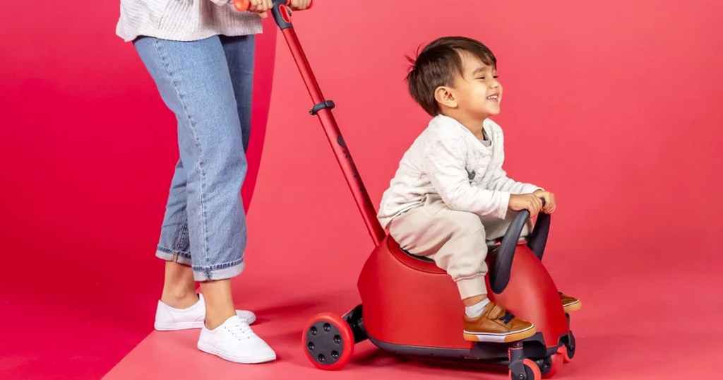 mom pushing child on a red ride-on toy