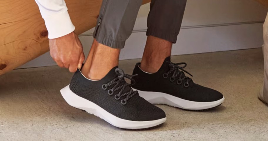 man putting on a pair of black allbirds shoes