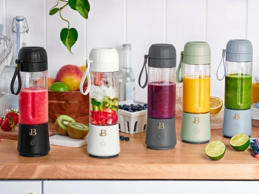 different color portable hand blenders filled with juices on a countertop with fruits 