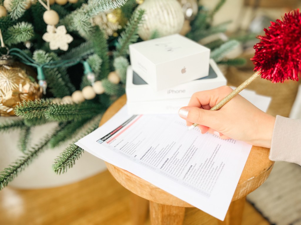 womans hand holding a festive pen writing on a printed sheet of paper in front of a christmas tree