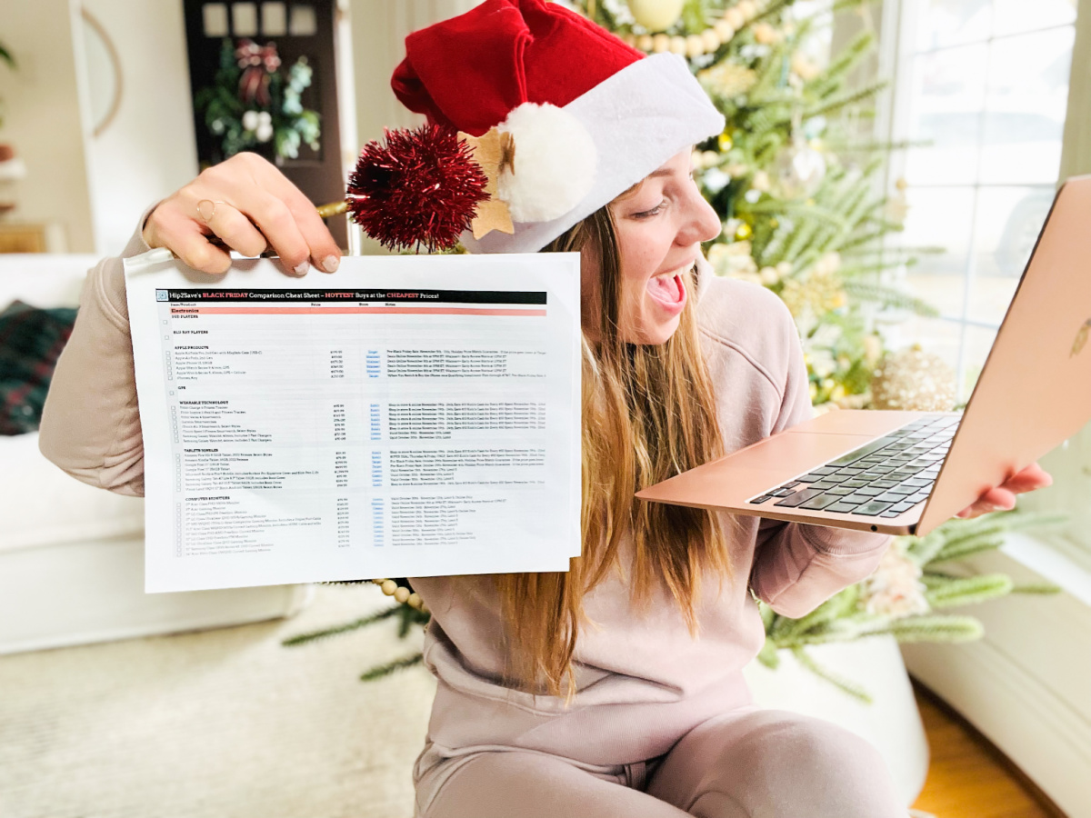 woman in a santa hat staring in awe at her laptop while holding a printed sheet of paper