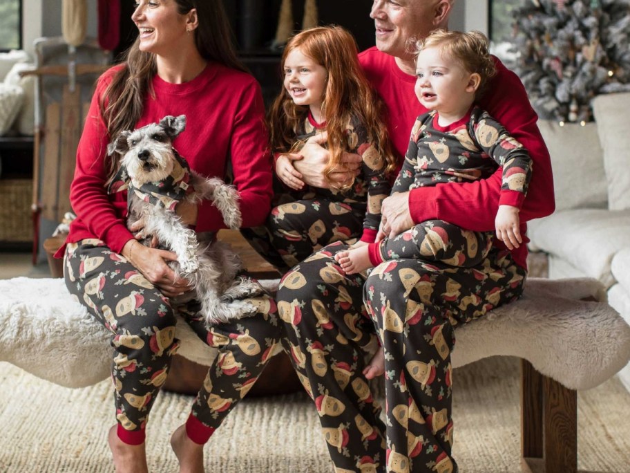 family sitting on a bench with a dog all wearing matching Christmas pajamas with reindeers on them