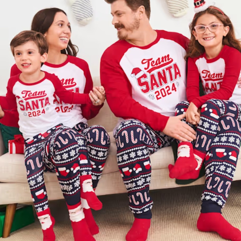 family sitting on a couch wearing matching blue, red and white Christmas pajamas that say 