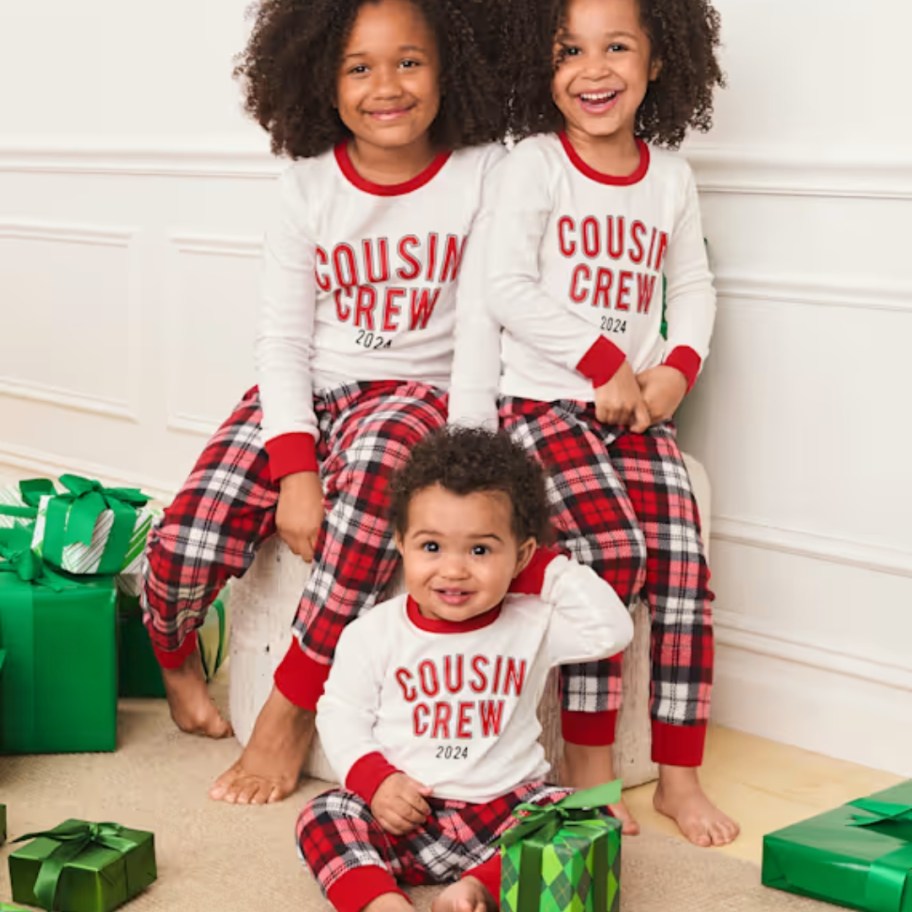 a baby and 2 little girls wearing matching red plaid and white long sleeve pajamas that say 