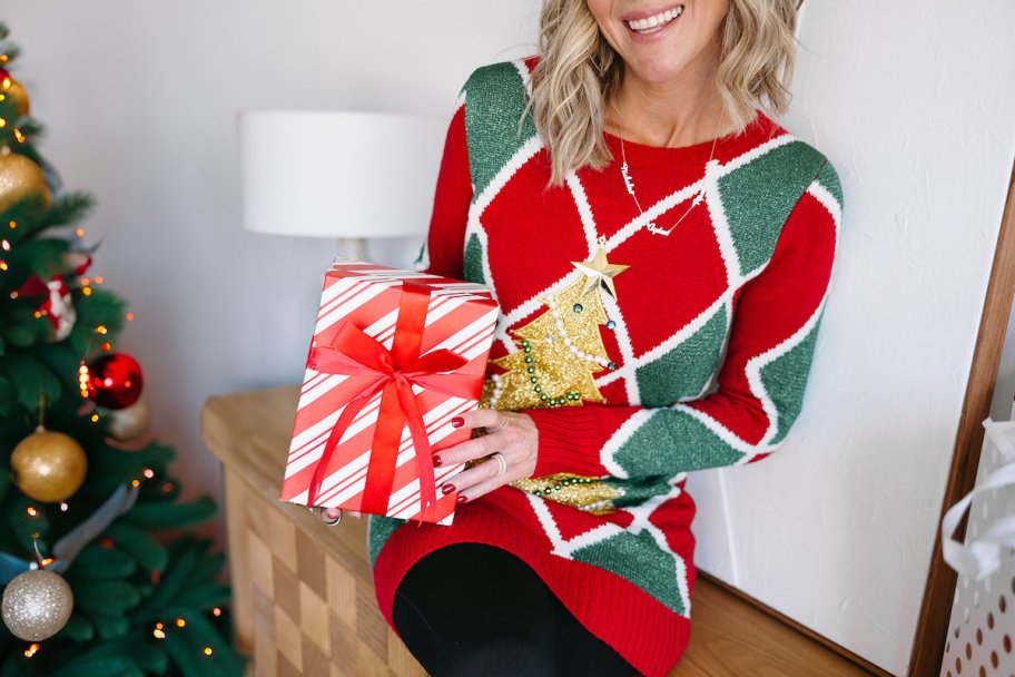 woman holding a red and white holiday present wearing a christmas sweater