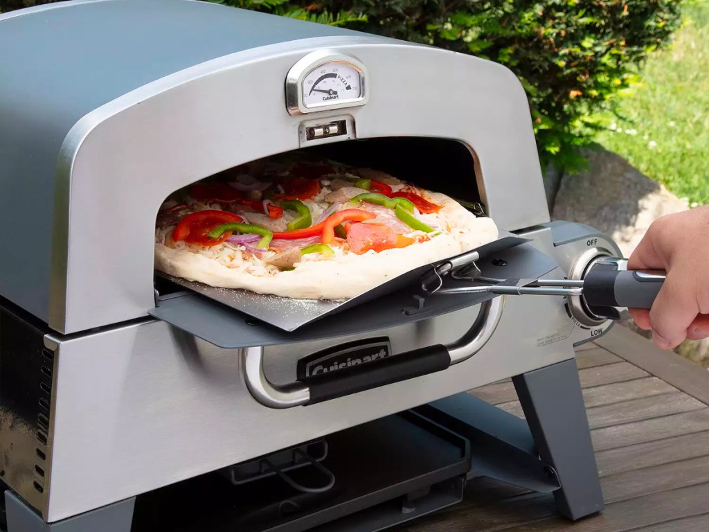 someone putting a pizza inside a cuisinart pizza oven on table