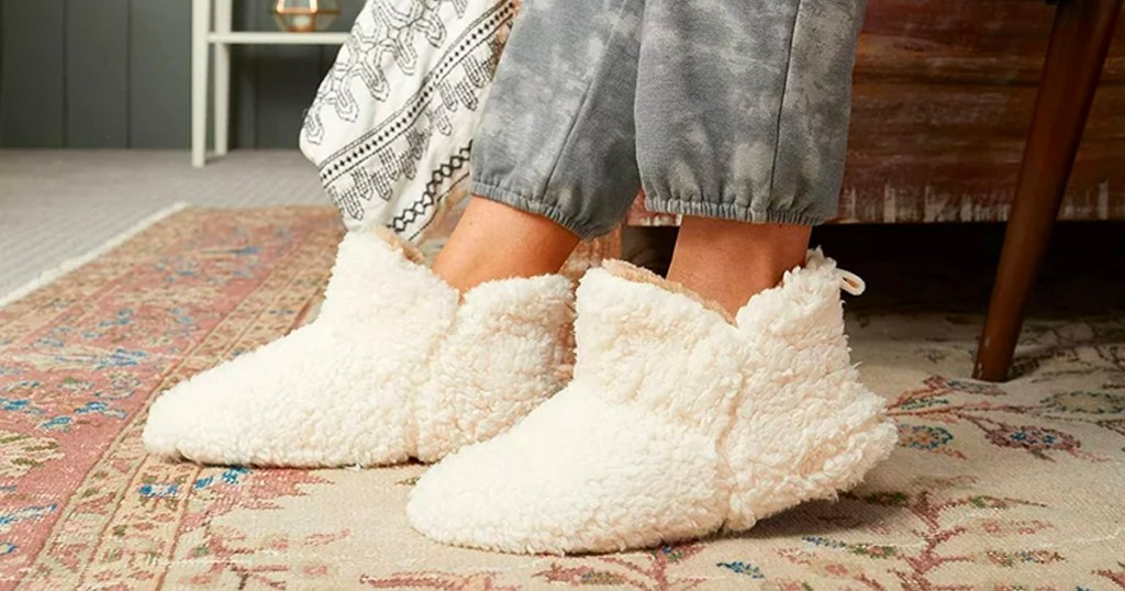 feet with white sherpa slippers on them on carpet