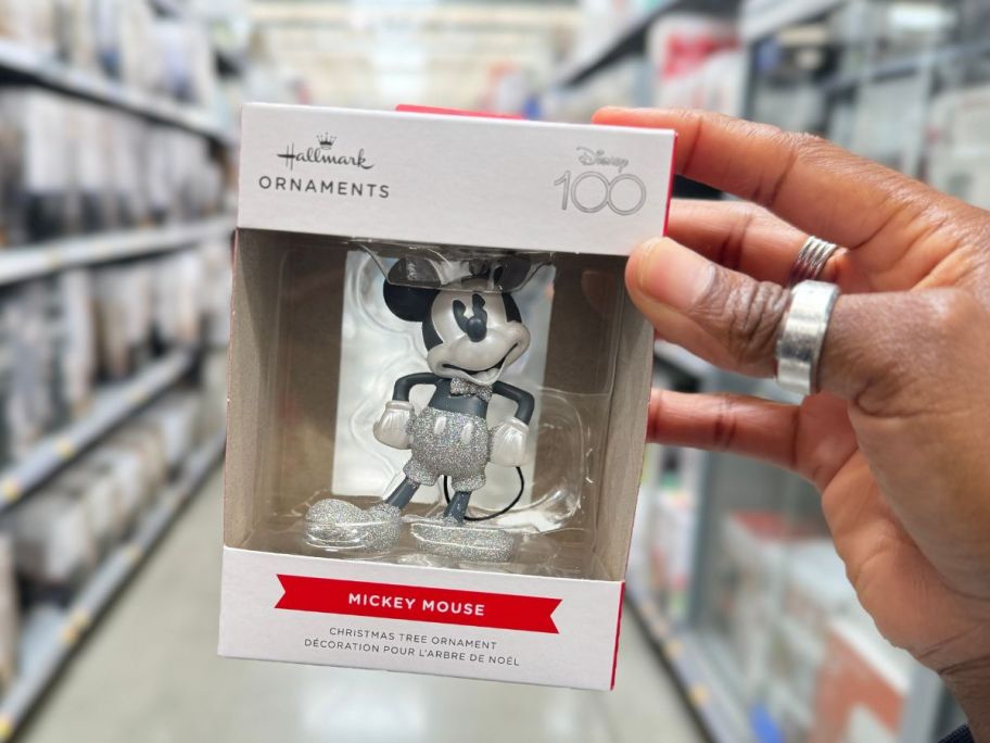 a womans hand holding a boxed mickey mouse ornament