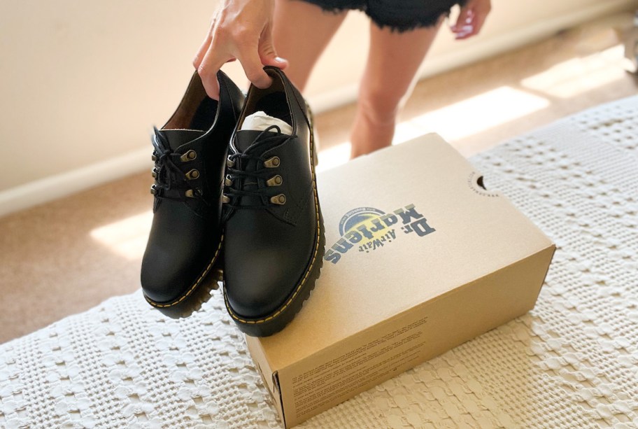 hand holding pair of black dr martens shoes with box