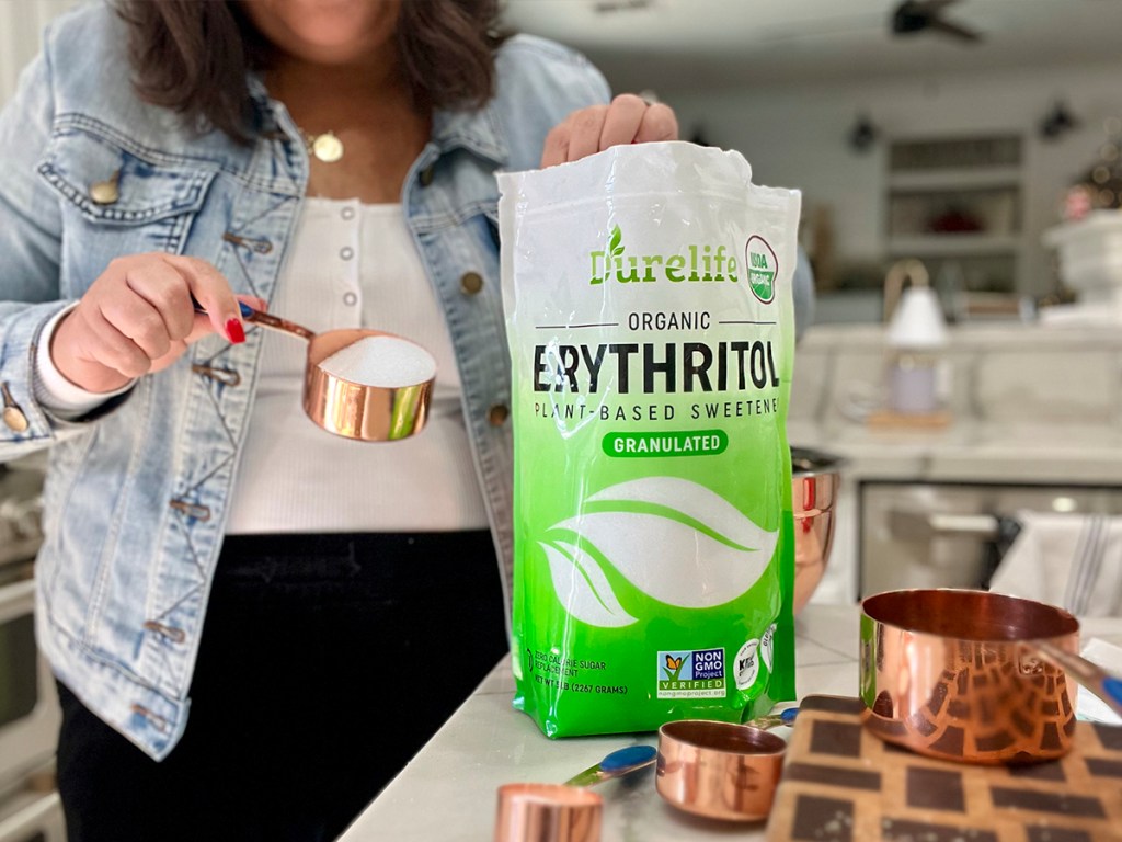 woman holding measuring cup full of sweetener next to bag of erythritol on counter