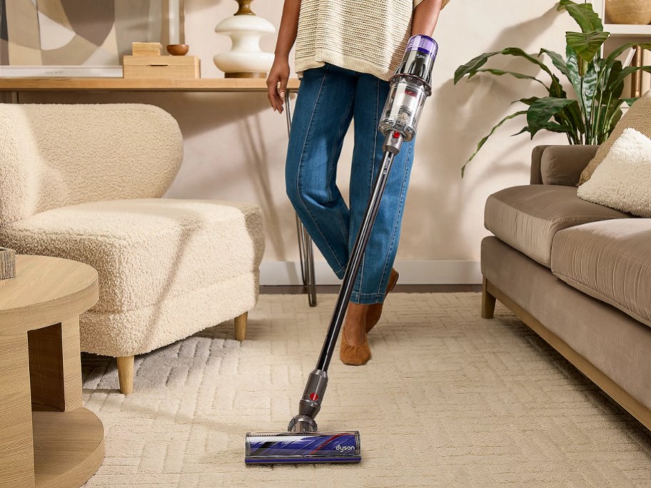 A person using a Dyson vacuum on a carpeted floor.