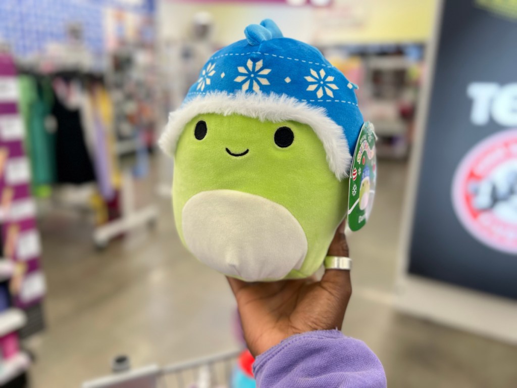 hand holding up a squishmallows dino in a five below store