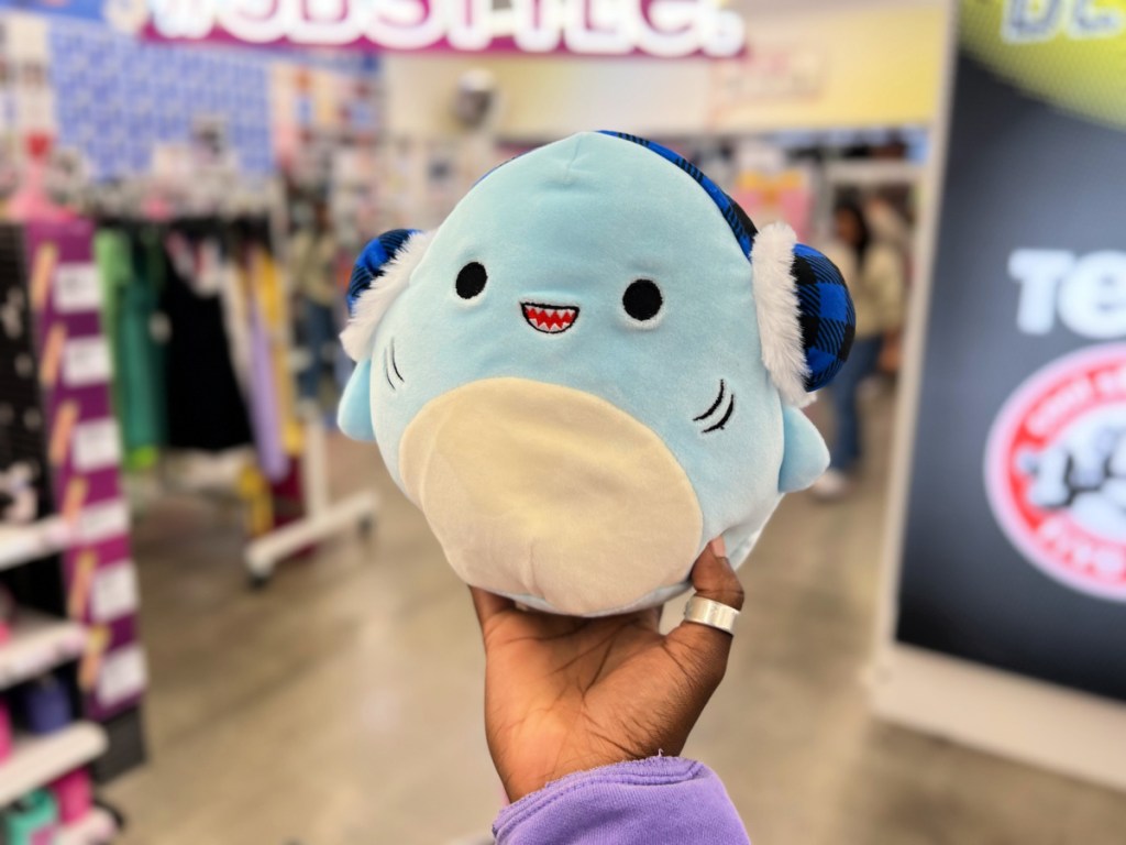 hand holding up a squishmallows shark wearing earmuffs in a five below store
