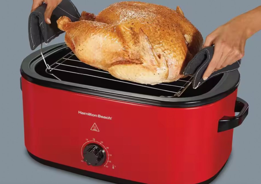 hands putting turkey in red roaster oven