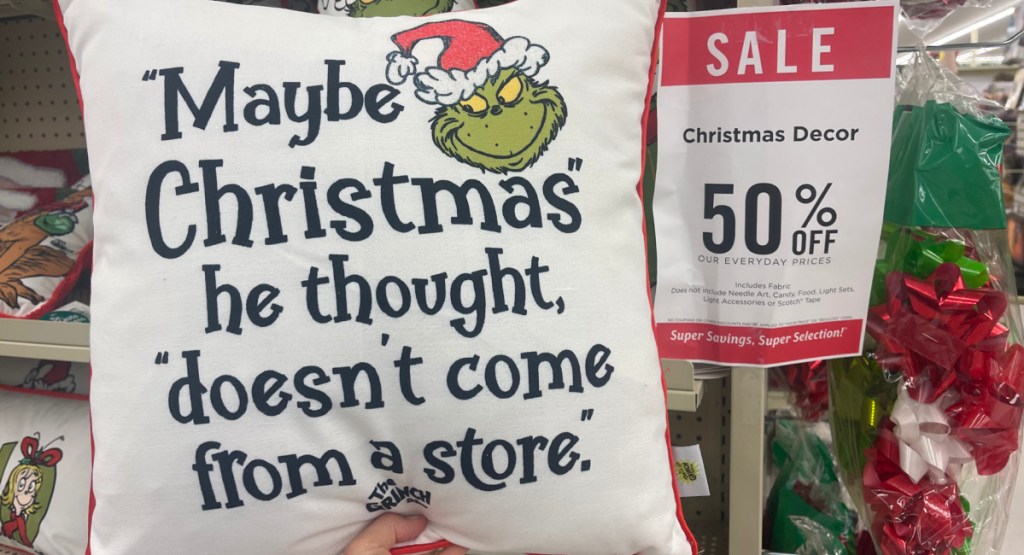 hand holding grinch throw pillow in front of 50% off Christmas decor sign