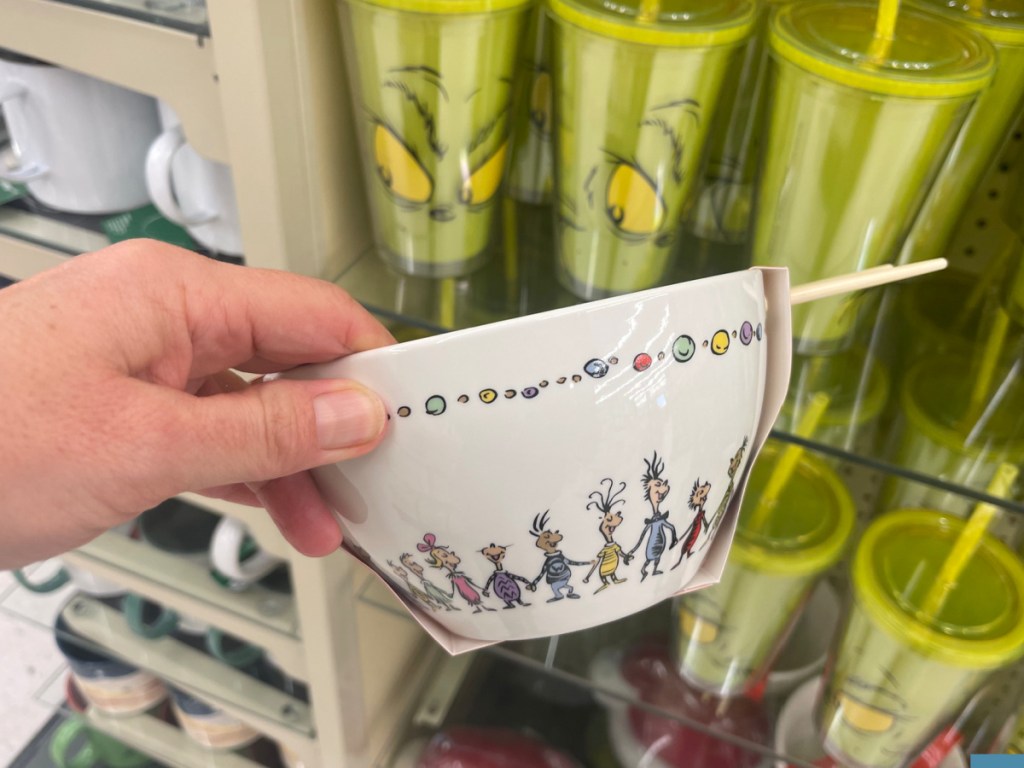 hand holding whoville bowl with chopsticks in front of a display of grinch tumblers