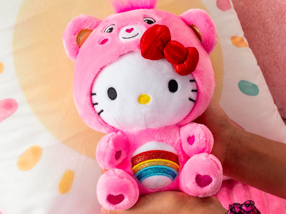 hands holding hello kitty dressed as care bear 