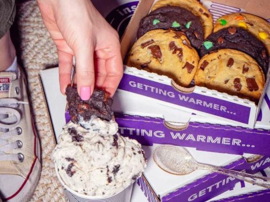 insomnia cookies ice cream in a cup with a hand dipping a cookies with a box of cookies next to it