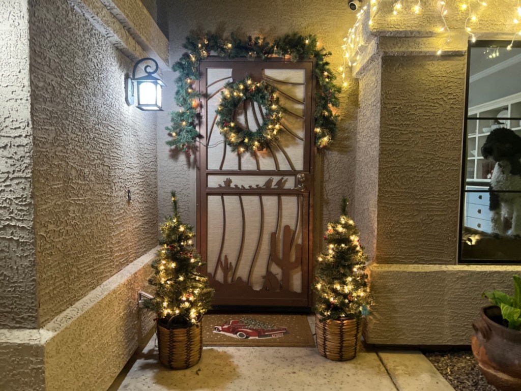 lighted wreath and swag above a door, with matching christmas trees on either side of the stoop