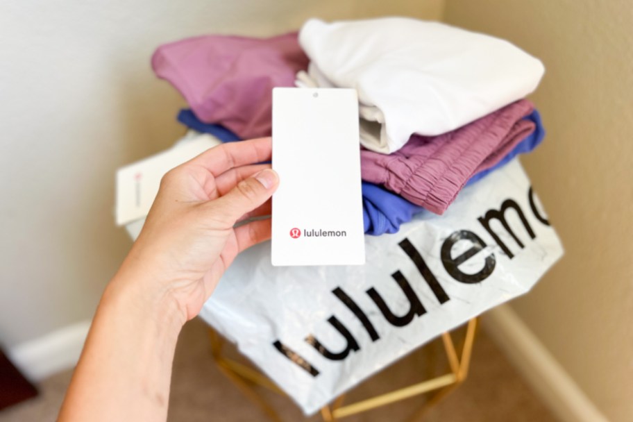 hand holding a lululemon tag with lululemon workout clothes and package behind it