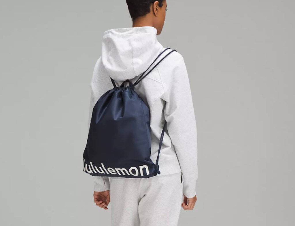 Teen wearing white sweatsuit with navy blue Lululemon drawstring bag on back 