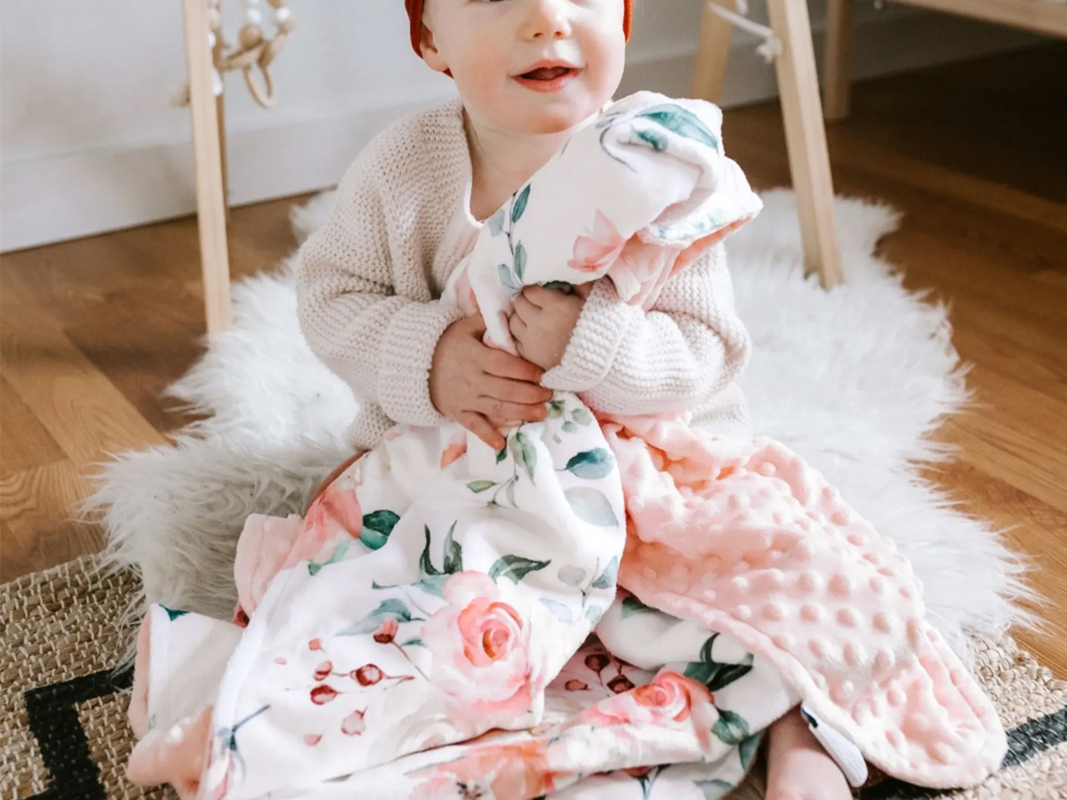 baby holding pink flower blanket