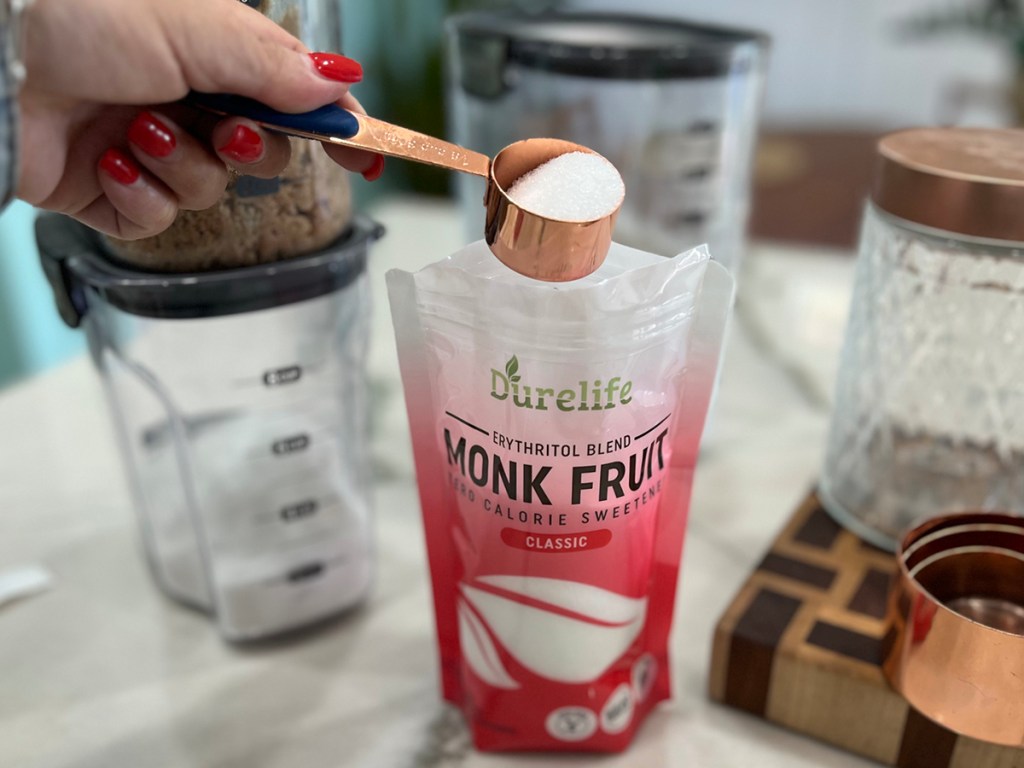 woman scooping sweetener with measuring cup out of bag of monk fruirt