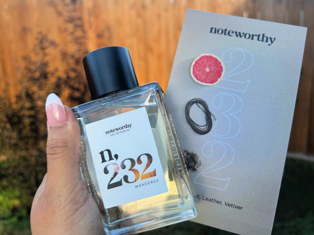 hand holding a bottle of noteworthy perfume with the card that talks about it