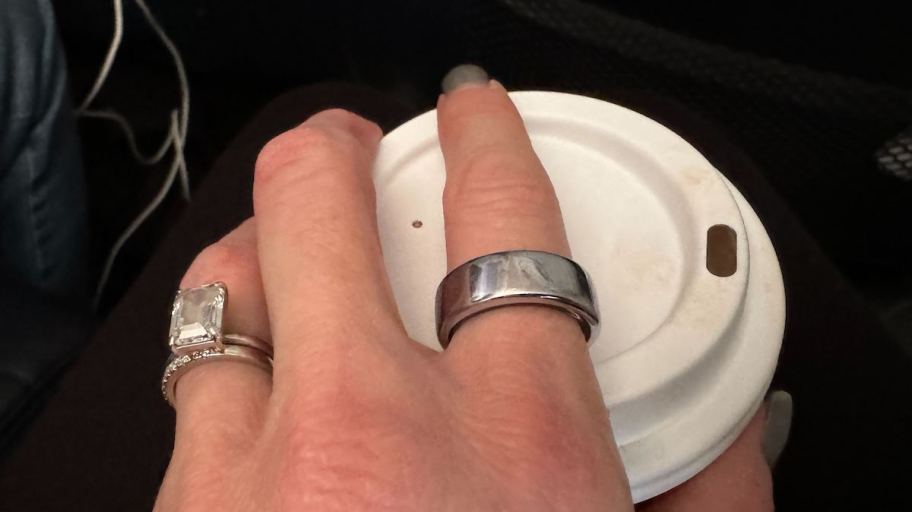 hand on top of coffee mug with oura ring and emerald cut diamond ring