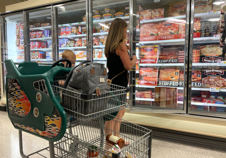 woman looking at pizzas in refrigerator in Publix store with shopping cart