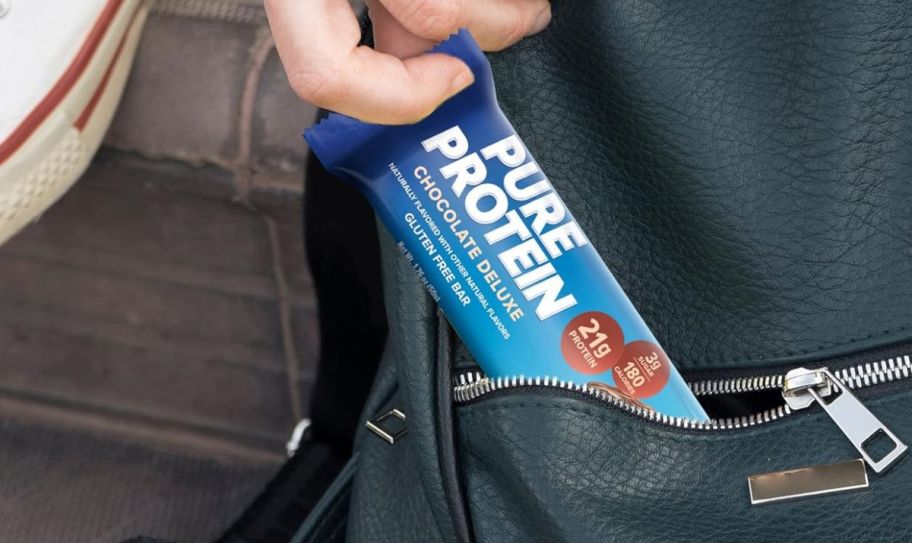 a hand removing a chocolate deluxe protein bar from a back pack