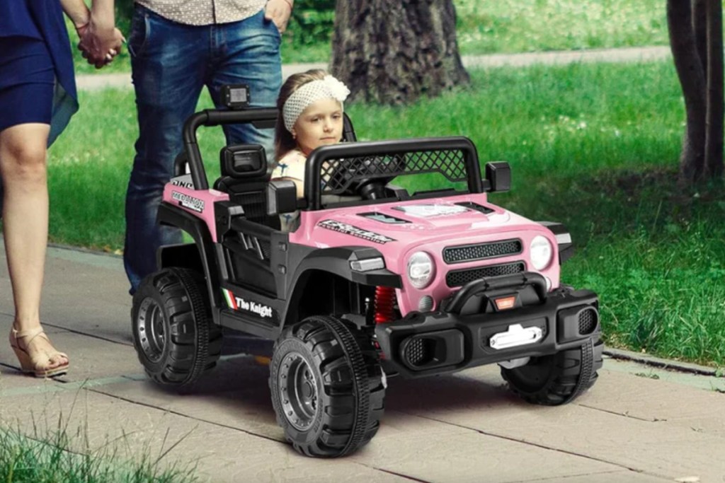 girl in pink 4 wheel drive ride on car next to parents