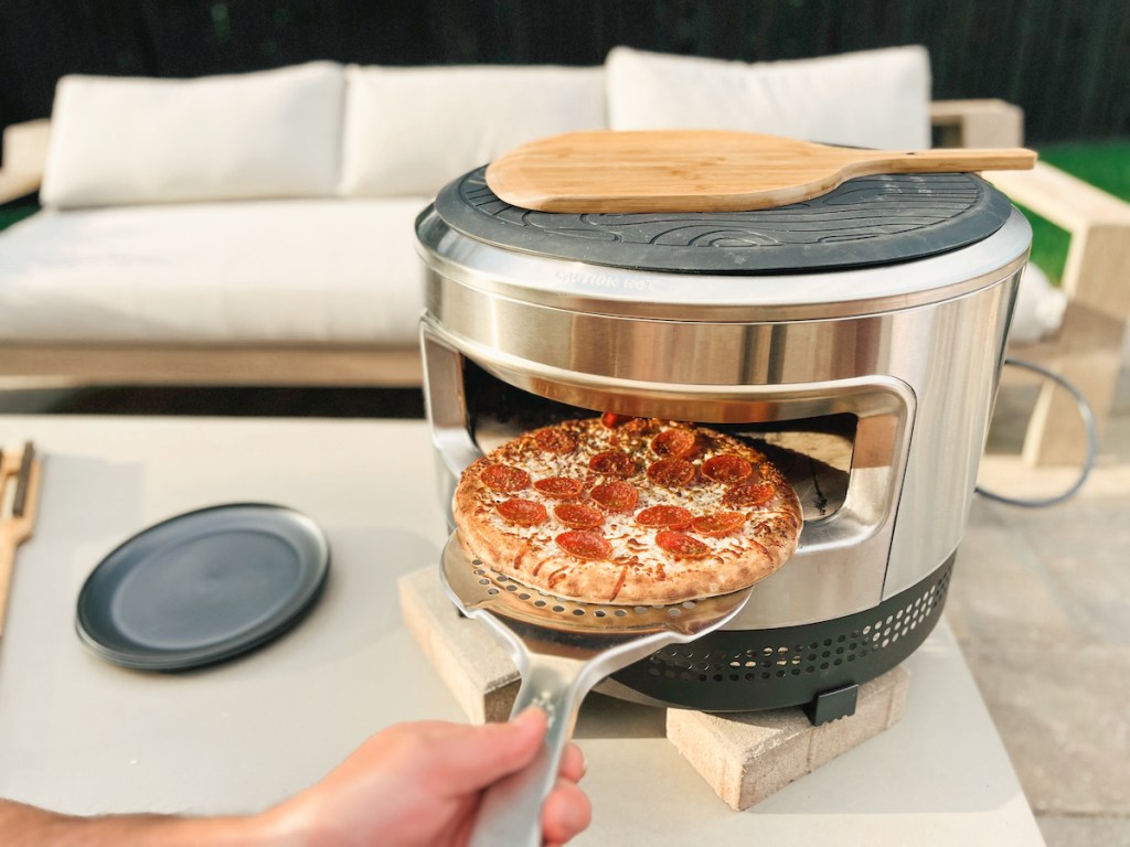 Person taking pepperoni pizza out of personal pizza oven
