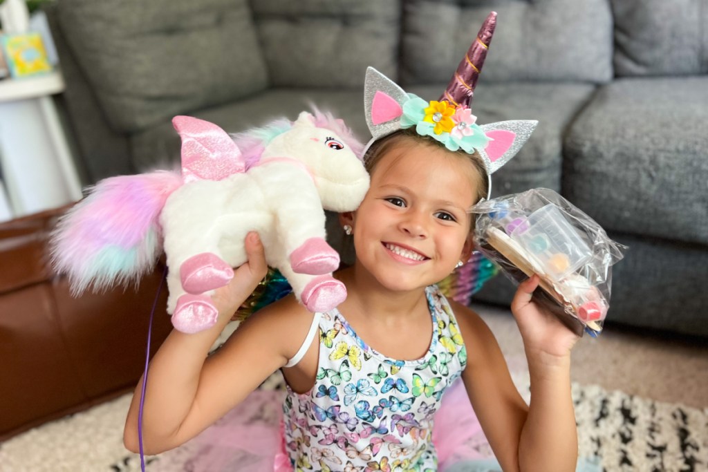 cheesing young girl wearing unicorn items and holding a plush unicorn toy