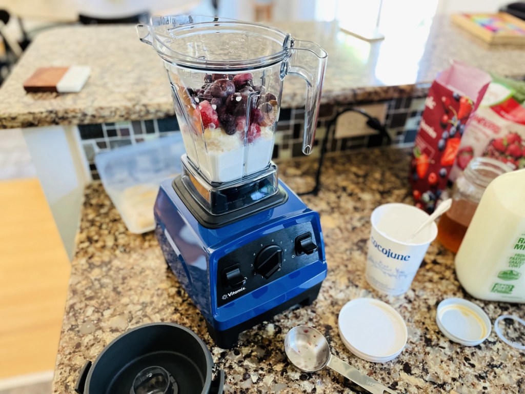 vitamix explorian 2.0 blender with fruit, milk and yogurt in it surrounded by smoothie ingredients