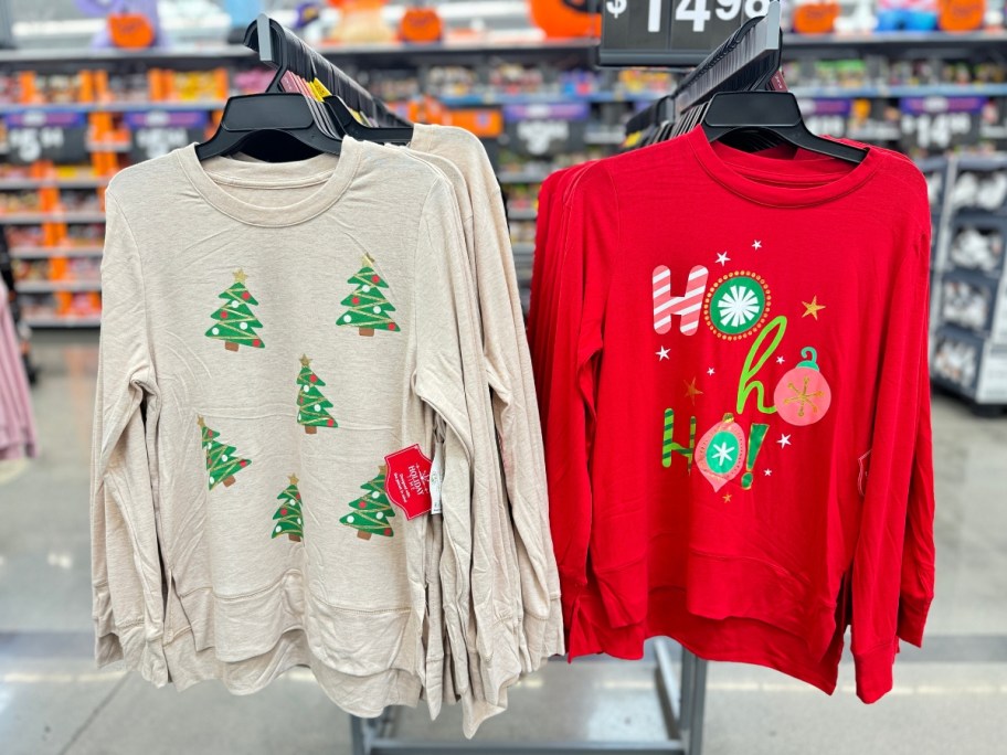 women's Christmas sweaters hanging from a Walmart cart, one cream with trees and one red with Ho, Ho, Ho