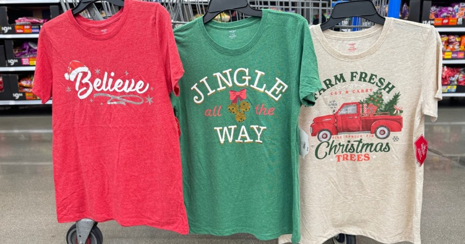 3 women's Christmas themed graphic t-shirts hanging on a Walmart shopping cart