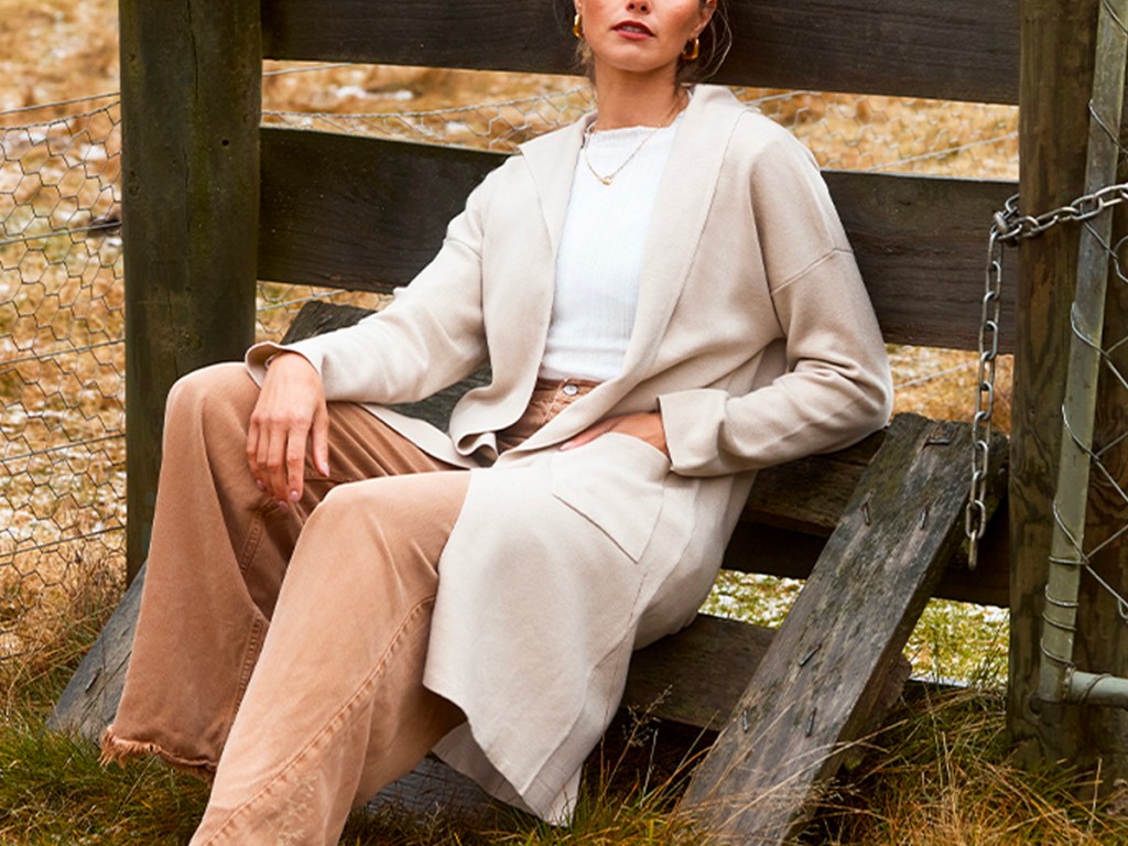 woman leaning near fence wearing biege cardigan