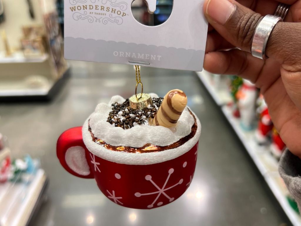 a womans hand displaying a wondershop hot cocoa ornament