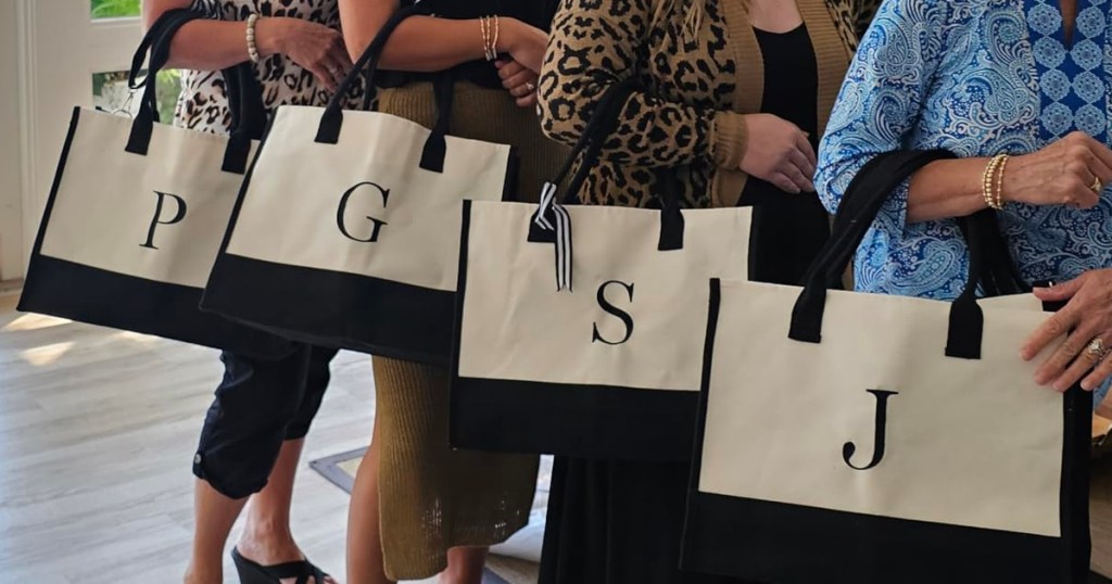 four women holding initial tote bags