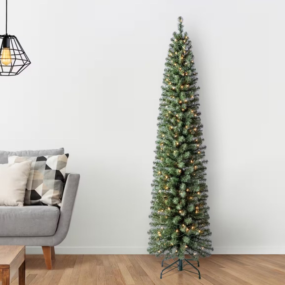 a slim pencil style artificial Christmas tree with clear lights in a living room