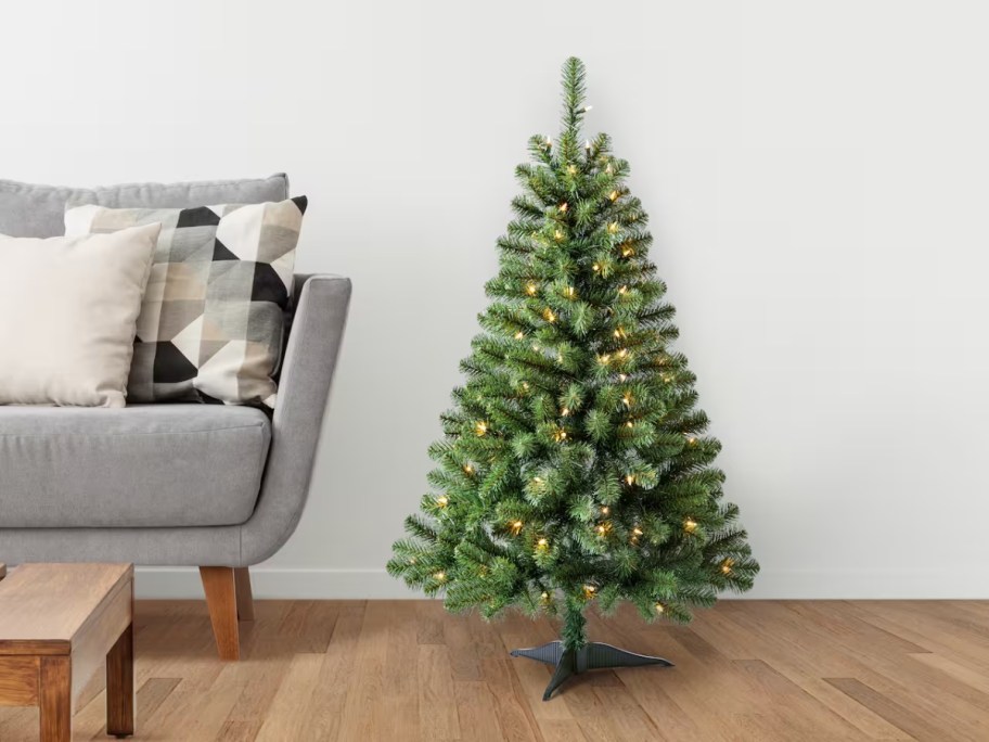 a 4 1/5 foot green artificial Christmas tree with clear lights in a living room