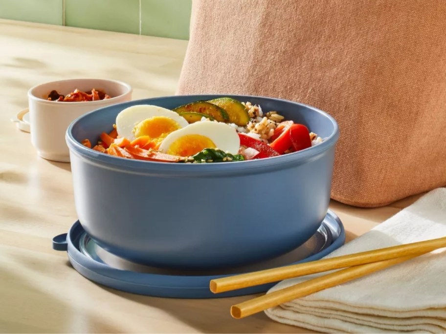 blue salad bowl with lid with salad in it on a counter next to a lunch bag