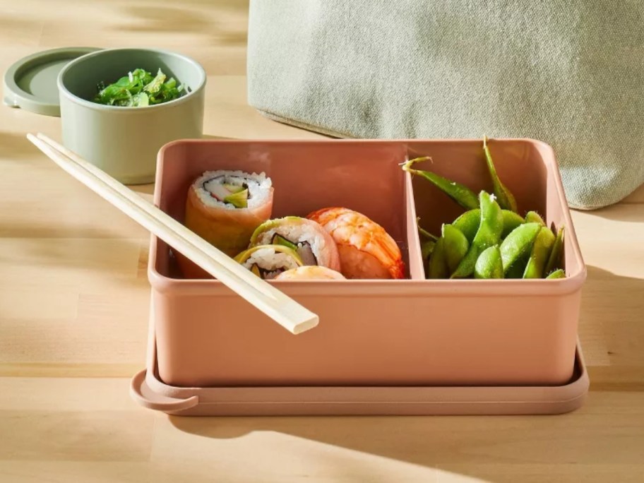 orange color bento box with food in it sitting on a counter next to a lunch bag