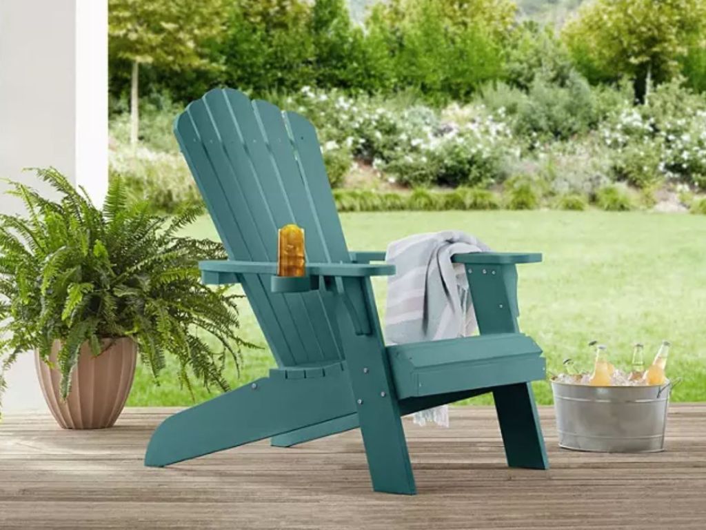 teal green Adirondack chair sitting on back deck with towel, drinks on the side, plants around it