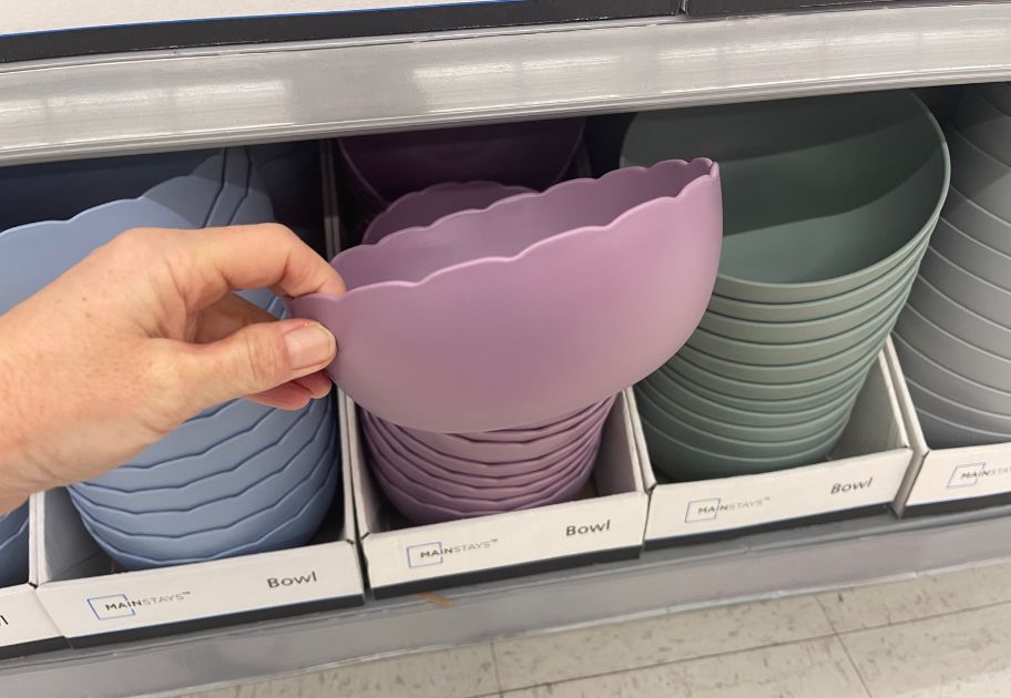 hand holding a lavender Mainstays Plastic Bowl with a scallop edge, other bowls in the background
