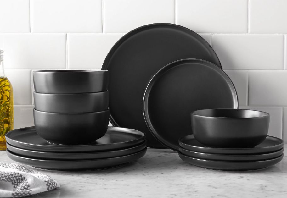 set of matte black stoneware dinnerware plates and bowls on a kitchen counter