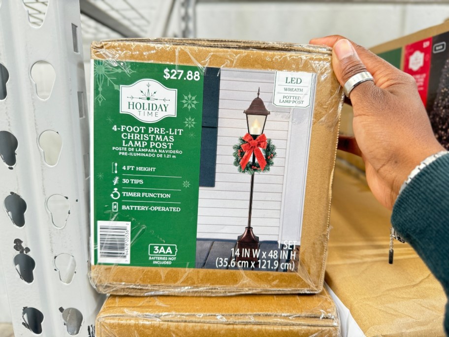 hand on a Holiday Time 4" Pre-Lit Christmas Lamp Post decoration in a box